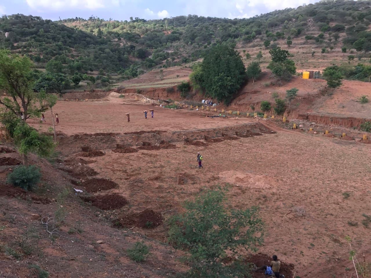 Aerial view of a bare hillside plot at TVC being reshaped with terraces, hills in the background.